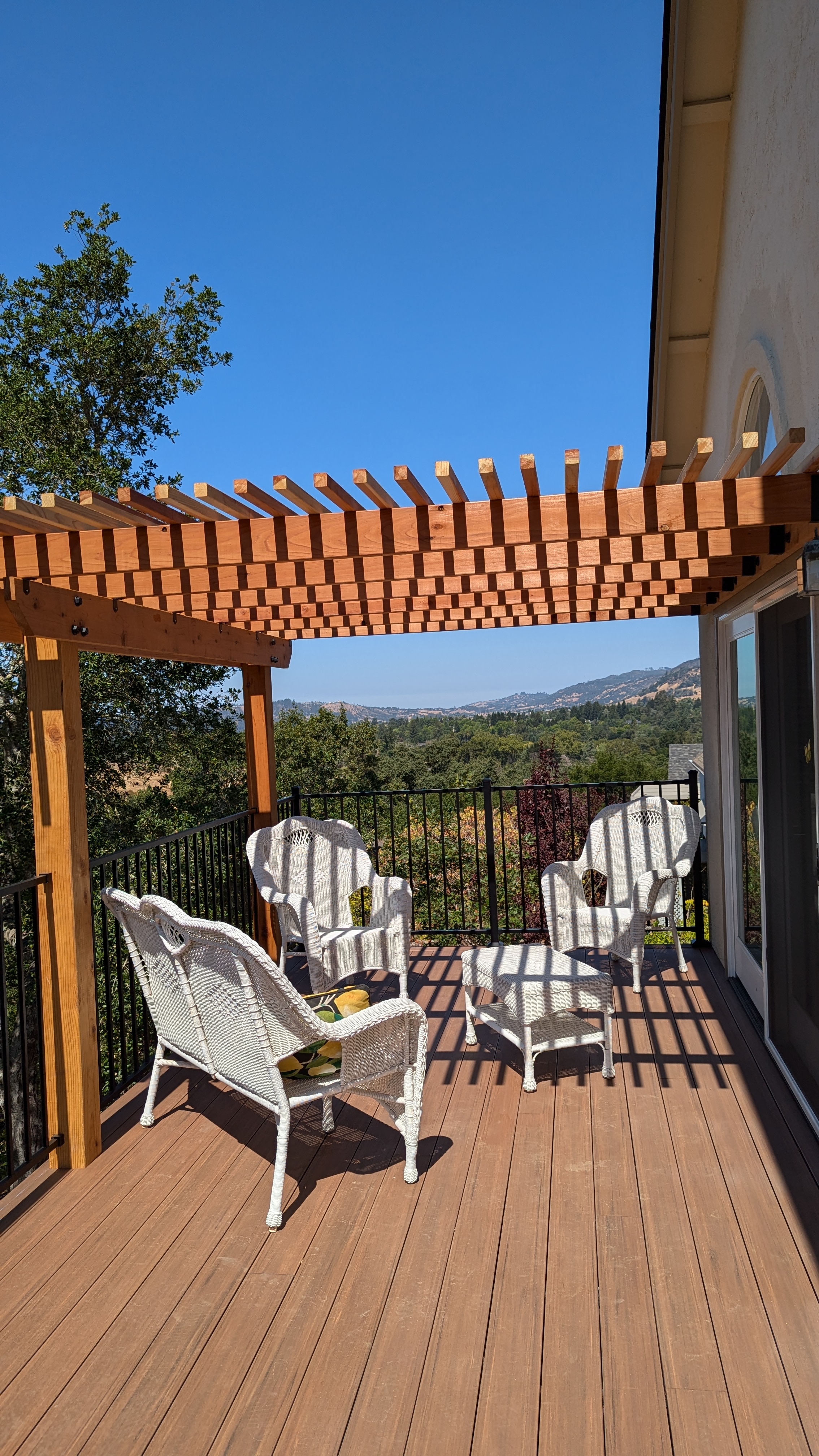 Composite deck with redwood pergola and black metal railing facing the hills